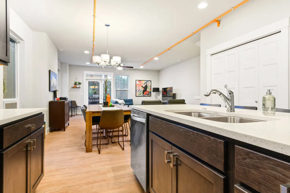 An open-concept kitchen, dining, and seating area adorned with artwork, providing a sense of warmth and sociability. The space offers ample room and a cozy ambiance, hinting at a comfortable spot for the whole family—including pets—to relax after outdoor activities.