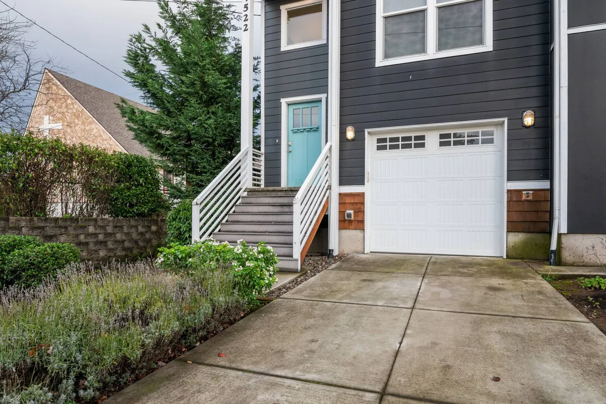 The image highlights the townhouse's front steps and garage door, framed by attractive landscaping. The focus on the entryway hints at welcoming guests and easy access to city life.