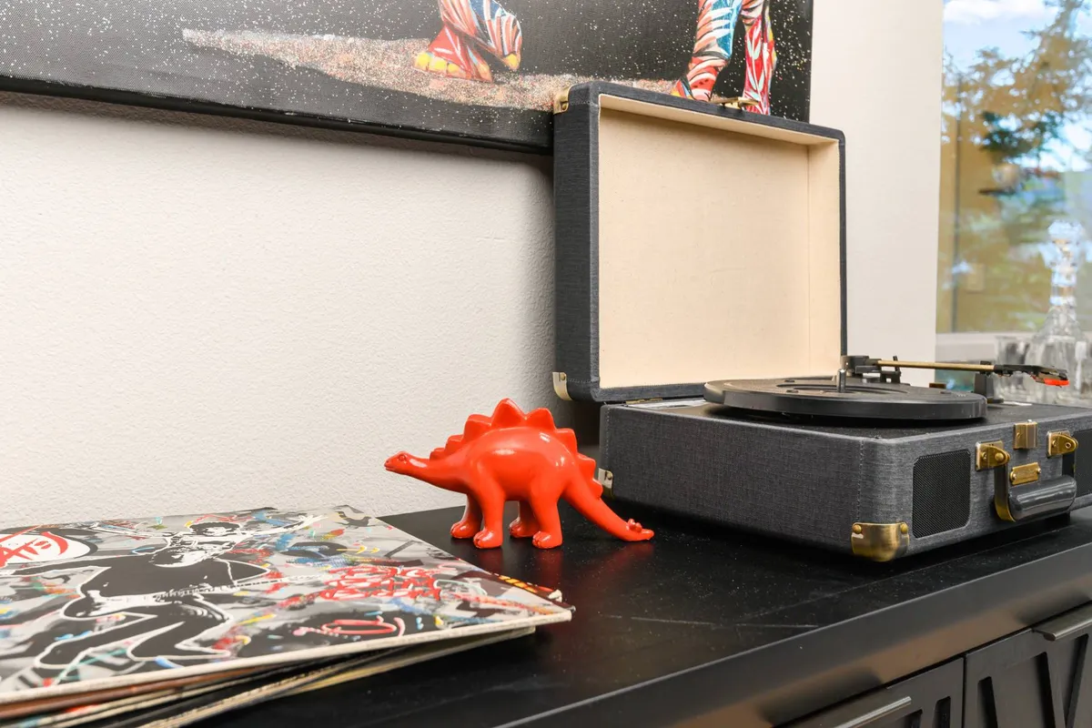 A cozy, creative corner featuring a record player, vibrant dinosaur figurine, and a stack of vintage records. The space exudes a playful, artistic vibe and hints at a love for local art and music.