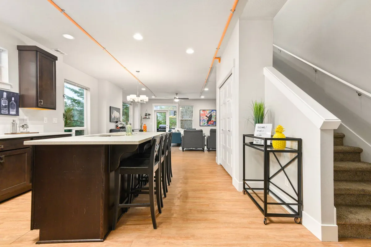 A modern, open-concept kitchen and dining area with a central island, inviting dining table, visible staircase, and curated wall art. The space is designed for seamless cooking, dining, and socializing, highlighted by contemporary fixtures and artistic decor.