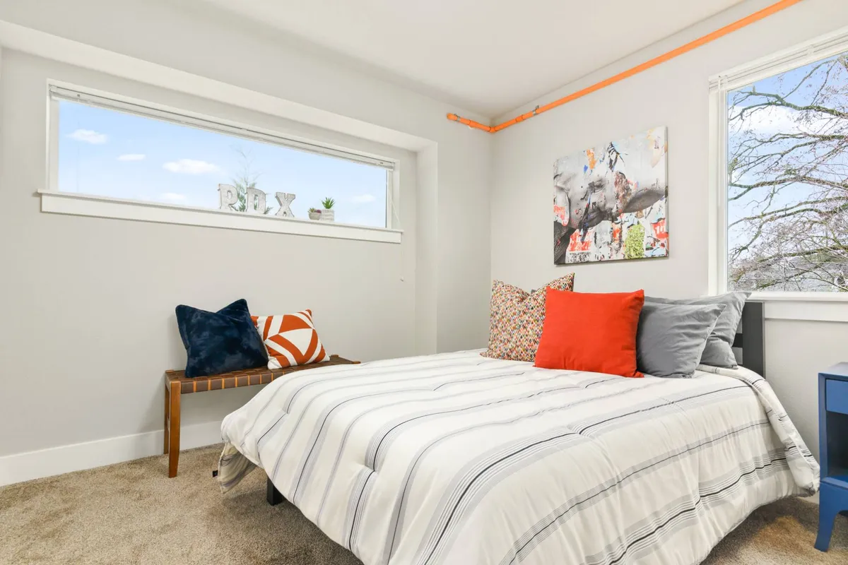 A relaxed bedroom setup with striped bedding, colorful throw pillows, wall art, and a window view, suggesting a comfortable and welcoming retreat after a busy day.