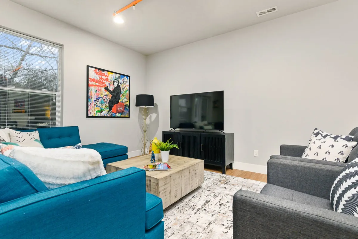 A comfortable living area with a plush turquoise couch, colorful artwork, a wooden coffee table, and a TV, set in an inviting, relaxed atmosphere. The space is perfect for relaxing, socializing, or quiet evenings in.