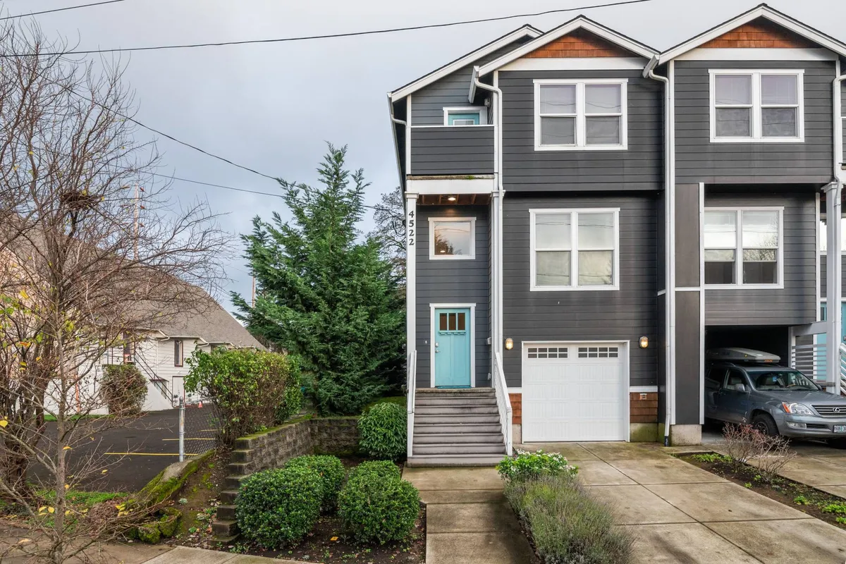 This image shows the exterior of a welcoming townhouse with a turquoise front door, gray siding, and a thoughtfully landscaped garden. The scene exudes a cozy, community-oriented atmosphere, suggesting a lively and inviting neighborhood.